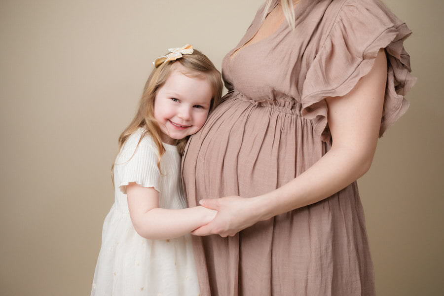 Toddler girl hugging her Mom's belly during their maternity photography session
