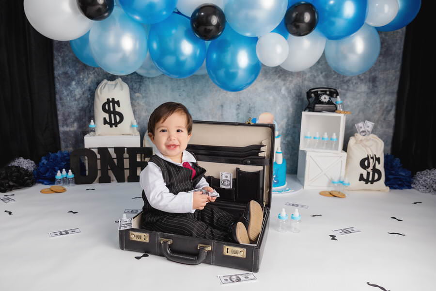 Baby Boss themed cake smash with a smiling baby boy in a suitcase