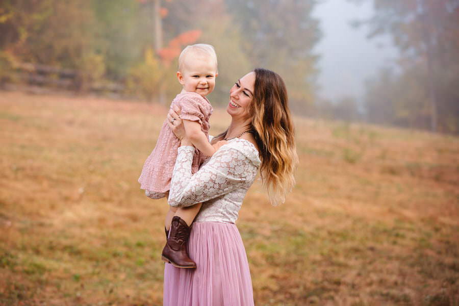 Mom in a mauve dress swinging her baby girl and smiling during their family photoshoot at their farm.