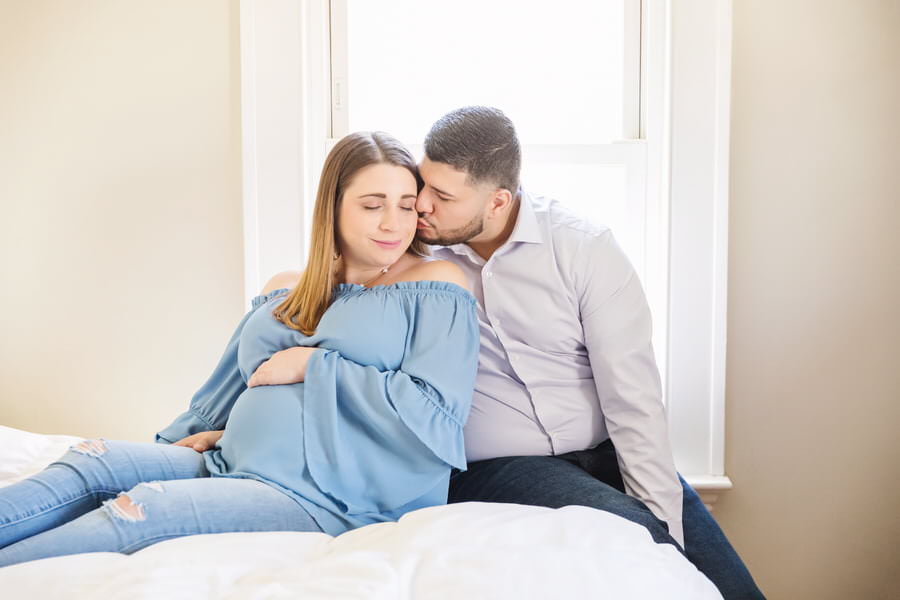 Husband kissing his wife on a bed during their in-home maternity photoshoot