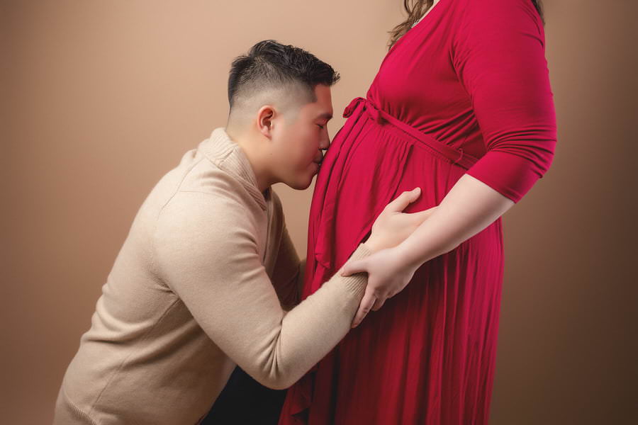 Husband kissing his wife's belly during their studio maternity photoshoot