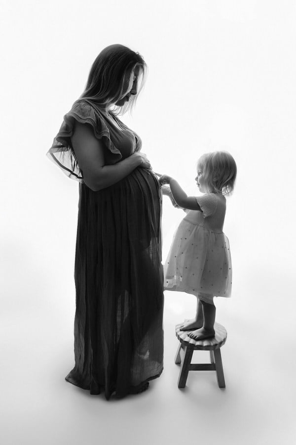 Mom & daughter posing against a backlit background during their studio maternity photoshoot