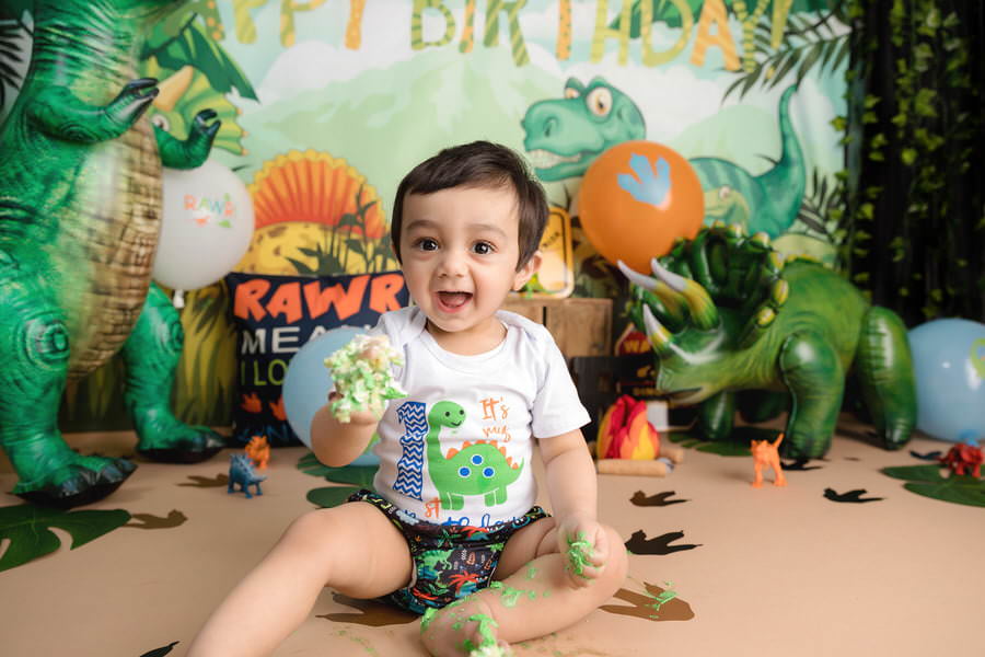 Smiling baby boy holding cake at his dinosaur cake smash photoshoot