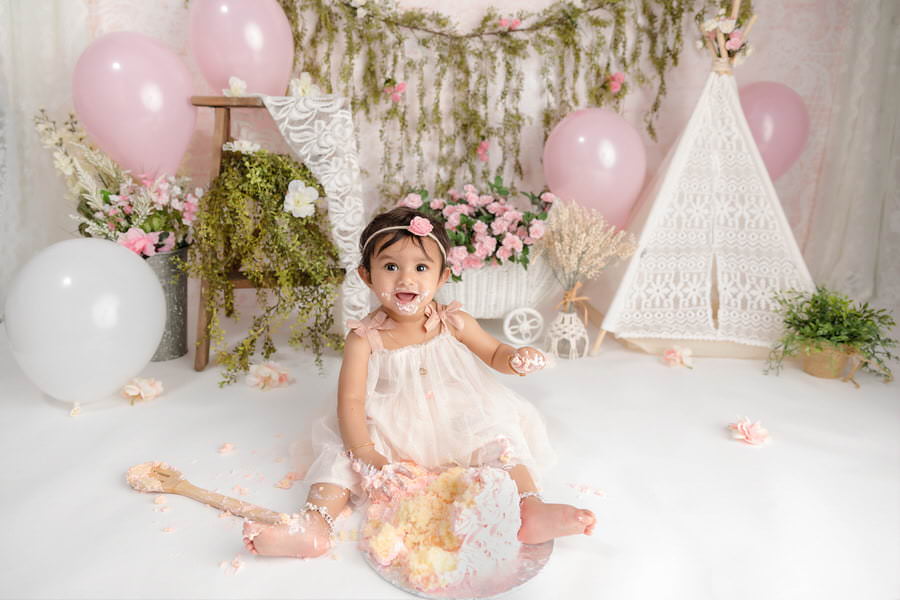 Smiling baby girl smashing her first birthday cake smash photoshoot, bohemian themed
