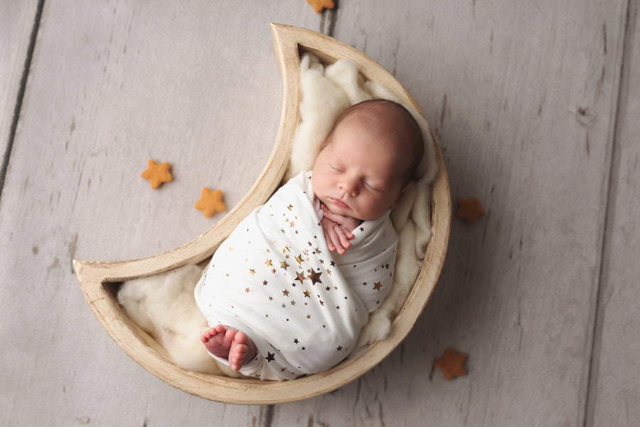 Sleeping newborn boy wrapped in a gold star white wrap lying in a moon prop during their photoshoot with The Flash Lady