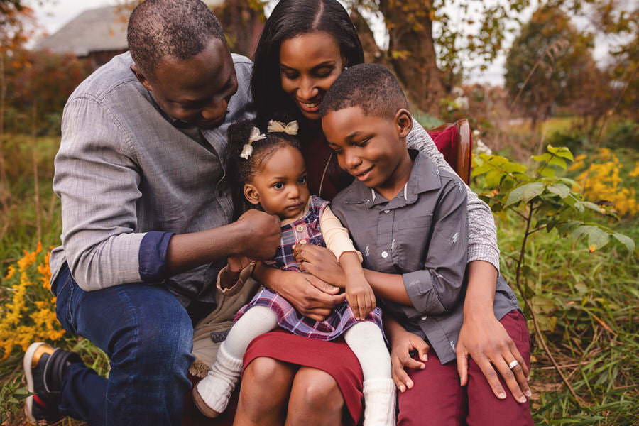 2 black parents snuggle with their daughter and son on a red chair during their family portraits