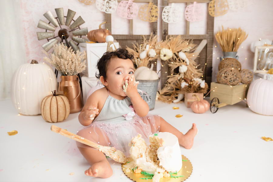 Baby girl eating cake during her pink pumpkin cake smash photography session