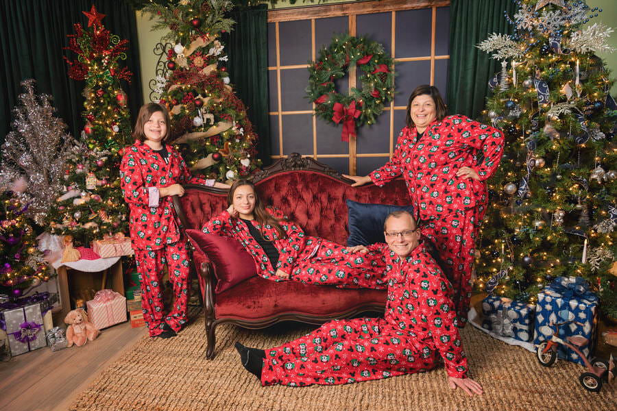 Mom and Dad with 2 teen daughters pose in matching Mickey Mouse pajamas in front of a Christmas scene at The Flash Lady Photography