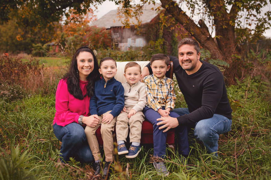 Family of 5 poses on a red chair with a barn behind them during their family photoshoot