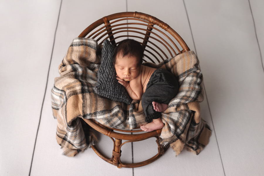 Sleeping newborn baby boy posing on a plaid black and tan blanket during his photoshoot with The Flash Lady