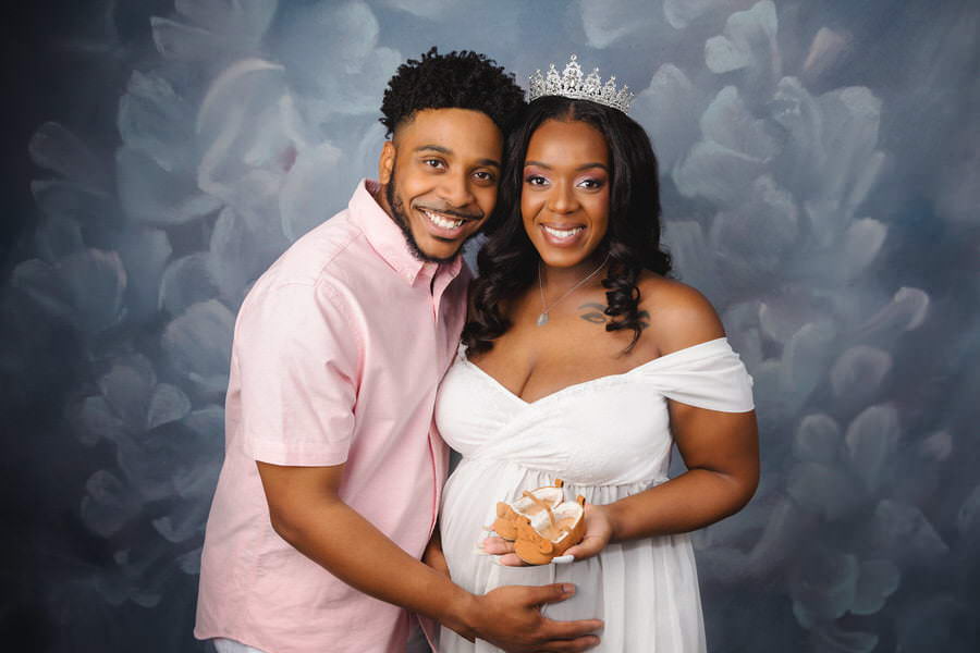 Smiling couple holding baby shoes during their maternity photoshoot