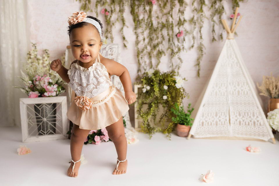 Black baby girl dances in a cream boho dress during her cake smash photos with The Flash Lady Photography
