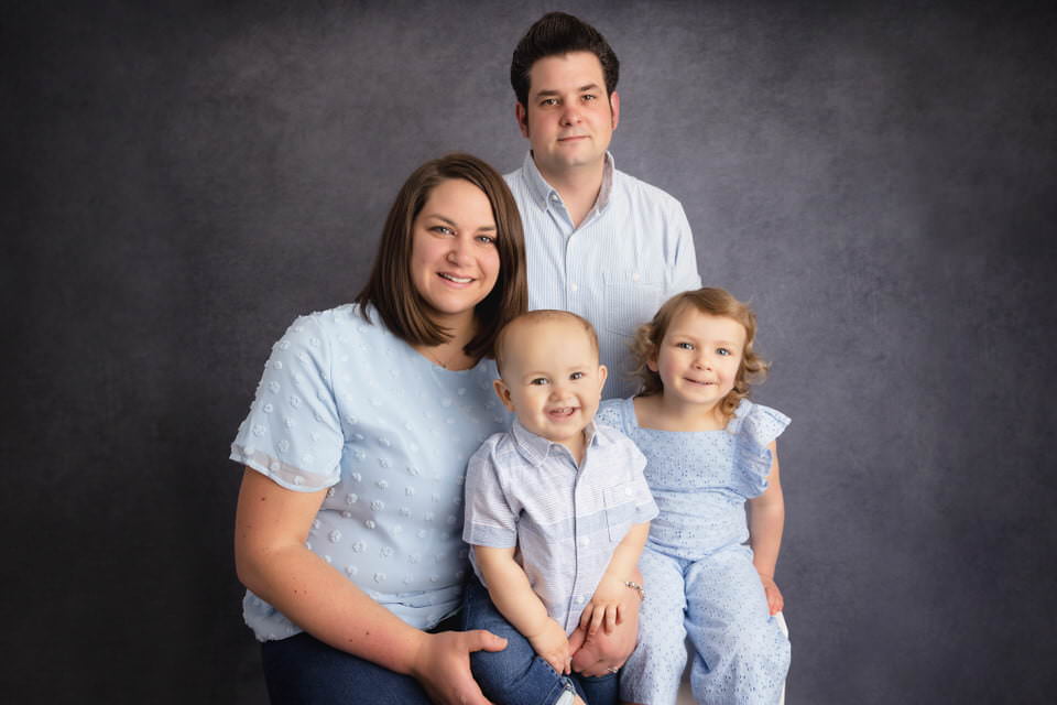 Husband and wife posing in studio with their 2 young children dressed in blue during their son's birthday photoshoot