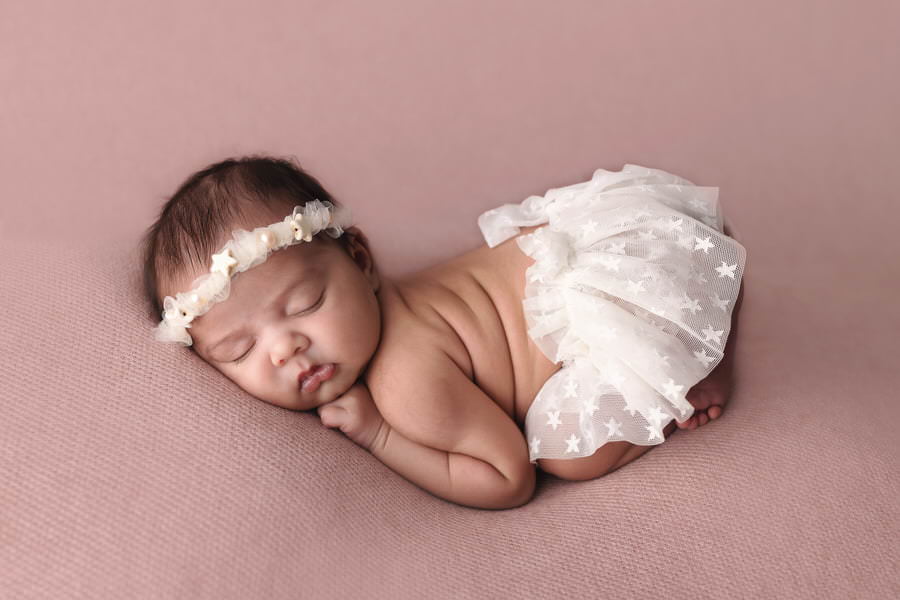 Sleeping baby girl in a white star skirt and headband posing on a pink blanket during her photoshoot with The Flash Lady
