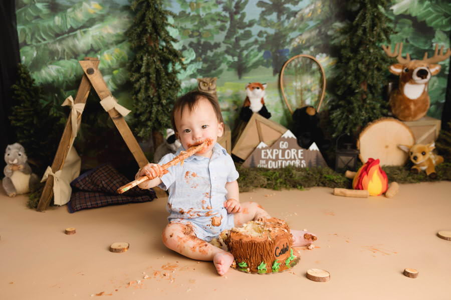 Toddler boy eating cake with a spoon for his cake smash photography session