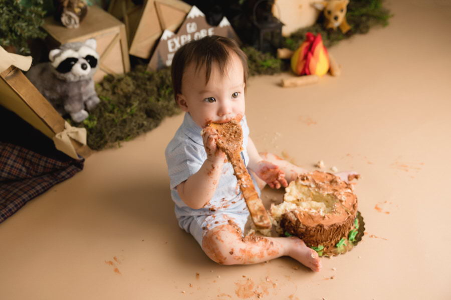 Baby boy eating his cake filled spoon during his cake smash photography session