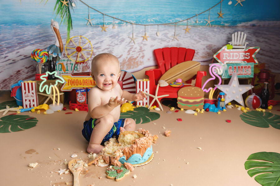 Smiling baby boy enjoying his first birthday with a seaside carnival cake smash photoshoot