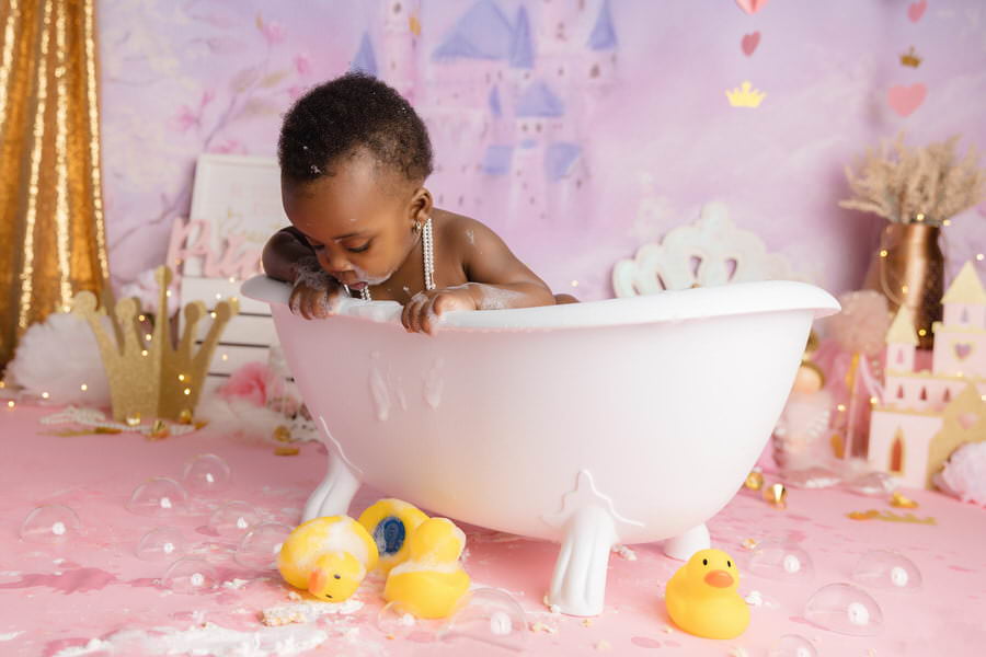 Baby girl looking at rubber ducks during her princess cake smash bath time..