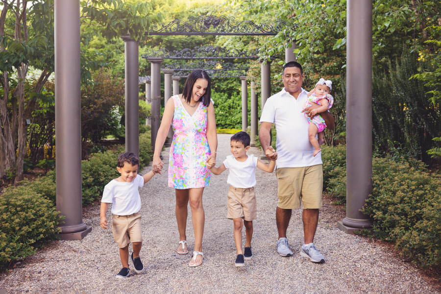 Hispanic family of 5 walks down a path with pillars during their family photoshoot