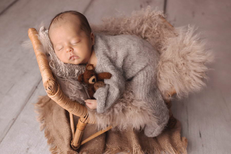 Sleeping newborn baby boy holding his teddy bear in brown pajamas posing on a curved prop during his photoshoot with The Flash Lady