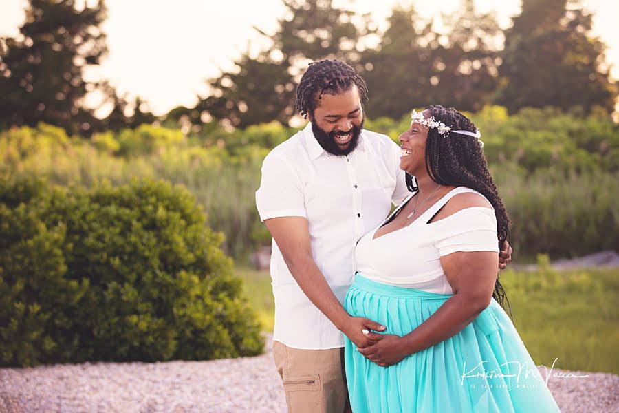 Laughing couple embracing Mom's pregnant belly during their beach maternity photos