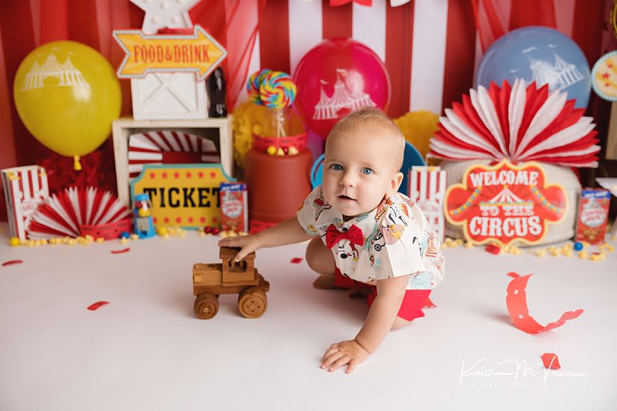 Baby boy sitting in front of his red and white carnival scene pushing a wood tractor
