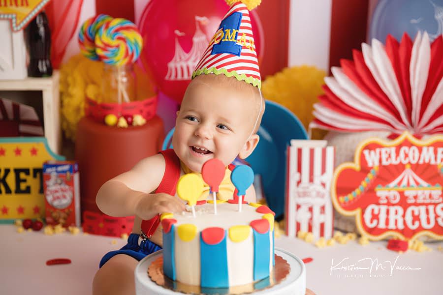 Smiling baby boy trying his cake during his colorful carnival cake smash photoshoot