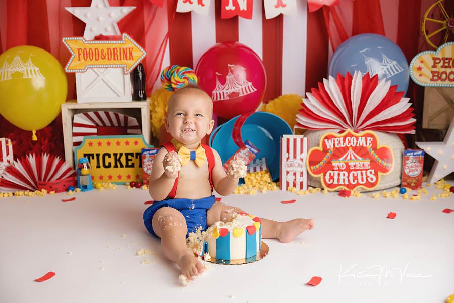 Excited baby boy smashing cake during his colorful carnival cake smash photoshoot
