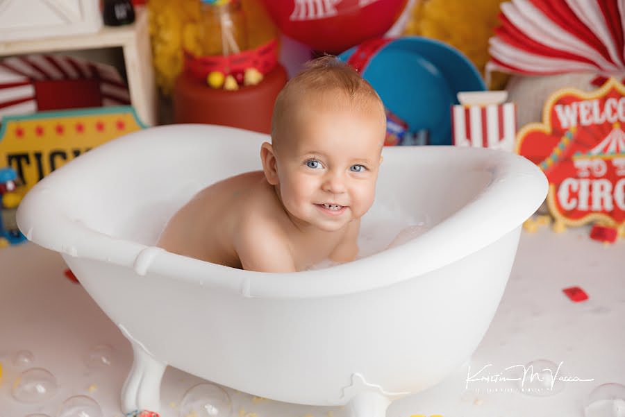 Smiling baby boy looking at the camera sitting in a bathtub during his cake smash photoshoot