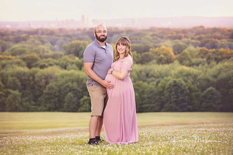 Smiling couple standing on top of a hill overlooking Hartford, CT during their maternity photos