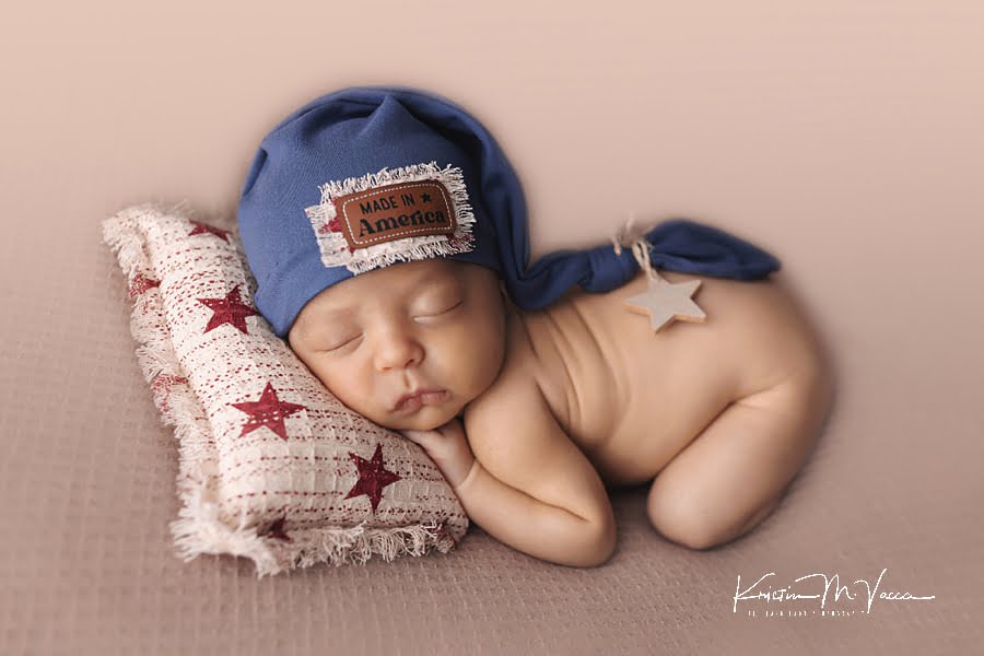 Sleeping baby boy on a red and white star pillow with blue hat posing during his July baby newborn photos
