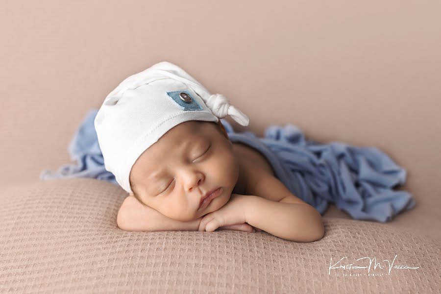 Sleeping newborn baby boy in a blue and white hat and wrap posing during his photoshoot