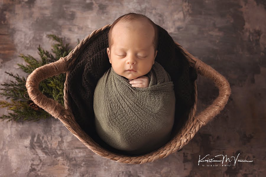 Sleeping infant boy wrapped in green lying in a brown basket during his July baby newborn photos
