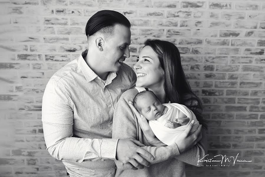 Black and white photo of husband and wife holding their new infant son wrapped in white