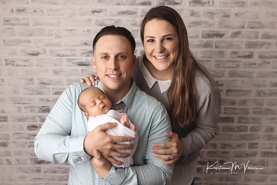 Smiling husband and wife holding their newborn son posing during their photoshoot