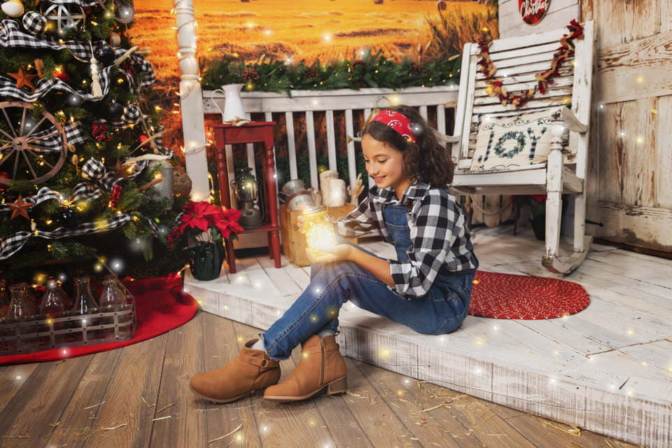 Smiling white girl in a black and white plaid shirt and overalls looking down at a jar of light during her Christmas photoshoot