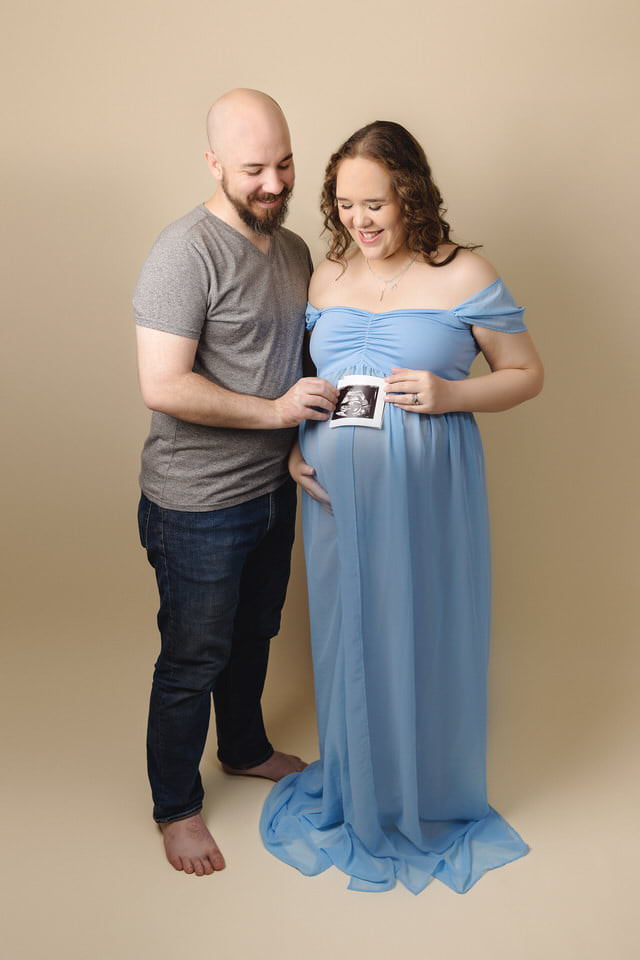 Husband and wife look down at the ultrasound photo on her belly during their maternity photoshoot
