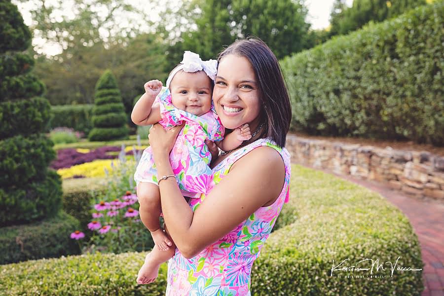 Mom holding baby daughter in matching floral dresses smiling outside during their happy family photos session