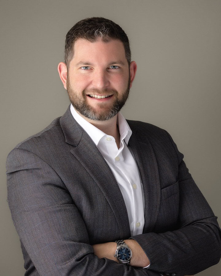 Smiling male lawyer with a beard posing in a gray suit for his professional headshot photoshoot by The Flash Lady
