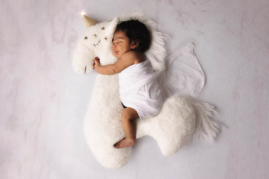 Sleeping newborn baby girl posing on a unicorn prop during her photoshoot with The Flash Lady