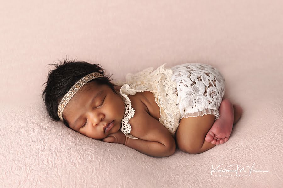 Beautiful newborn photography of a black baby girl posing in a white lace romper on a pink blanket by The Flash Lady