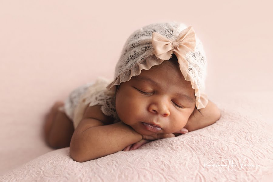 Sleeping black newborn girl in a cream hat posing on a pink blanket during her photoshoot by The Flash Lady