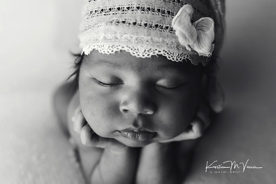 Black and white photo closeup of a black newborn girl with her hands under her chin during her photoshoot