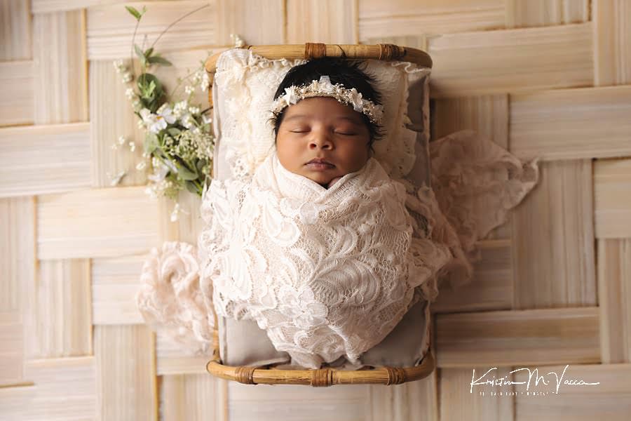 Sleeping black baby girl in a white lace wrap in a bed during her photoshoot by The Flash Lady