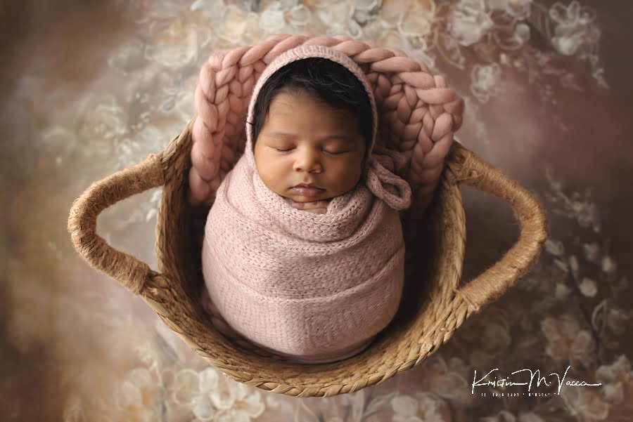 Black baby girl sleeping wrapped in pink on a floral background during her newborn photography session