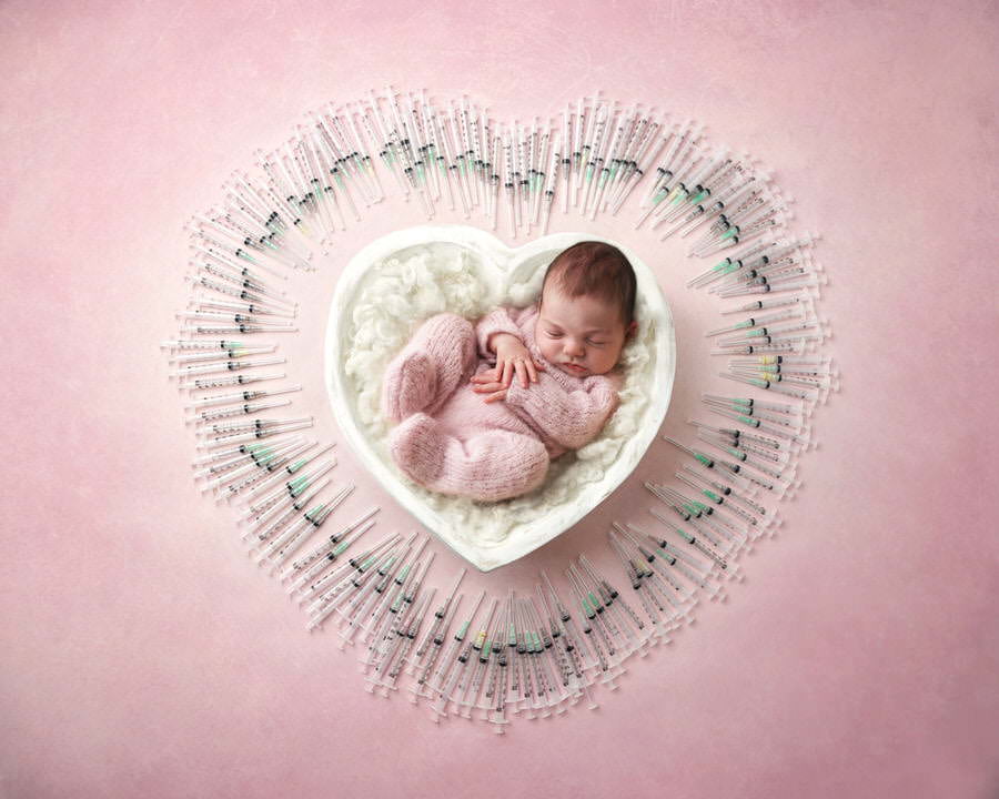 Sleeping newborn baby girl in a white heart bowl surrounded by IVF needles during her photoshoot