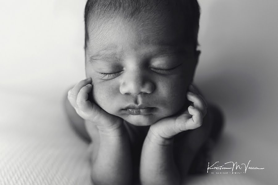 Black and white photo of an Indian newborn boy posing with his hands under his chin
