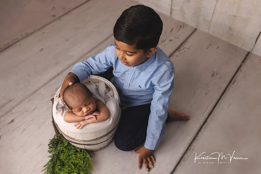 Newborn photos with older brother as he looks down on baby sleeping in a white bucket