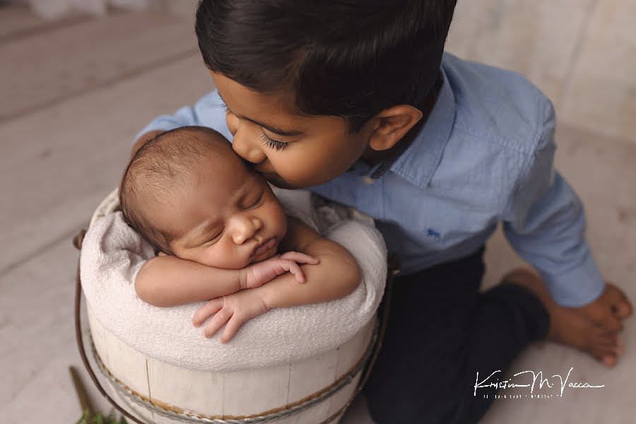 Indian big brother kissing his newborn baby brother on the head sleeping in a bucket during his photoshoot