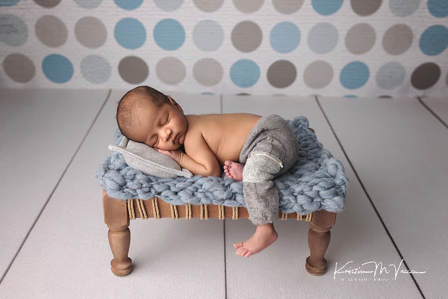 Sleeping Indian baby boy posing on a blue blanket and brown platform against a polka dot backdrop during his photoshoot